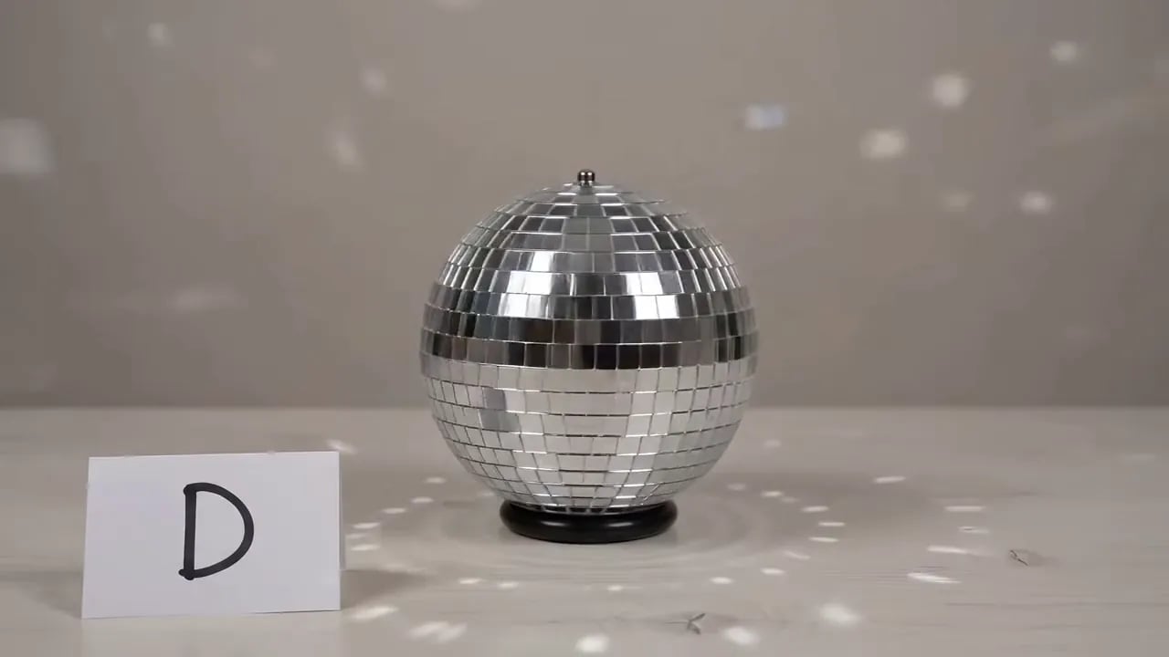 A disco ball sits on a table beside a handwritten card showing the letter D.