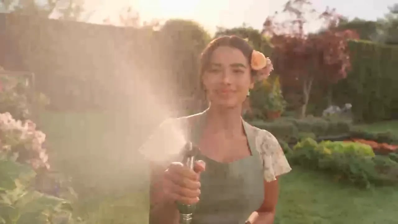 Dew-covered grass with a ladybug and a bee, then a smiling gardener spraying a mist of water from a hose.
