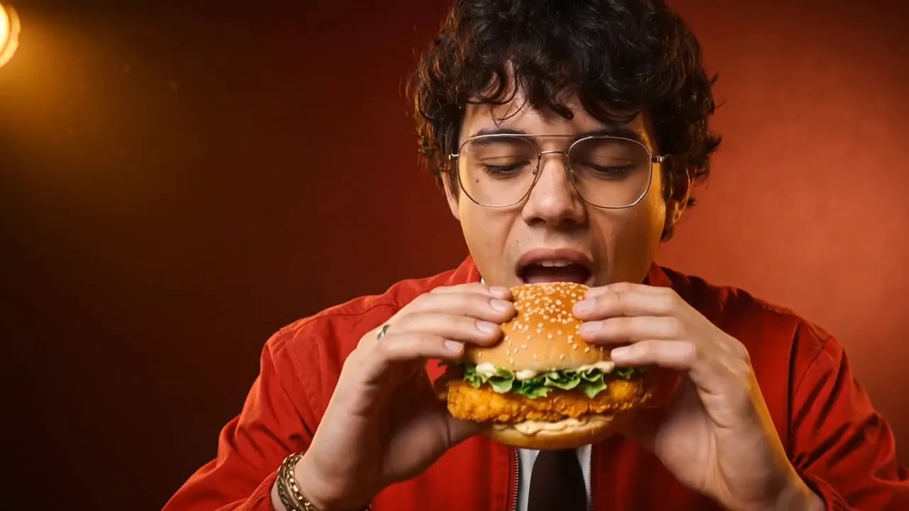 A man in glasses bites into a crispy chicken burger.