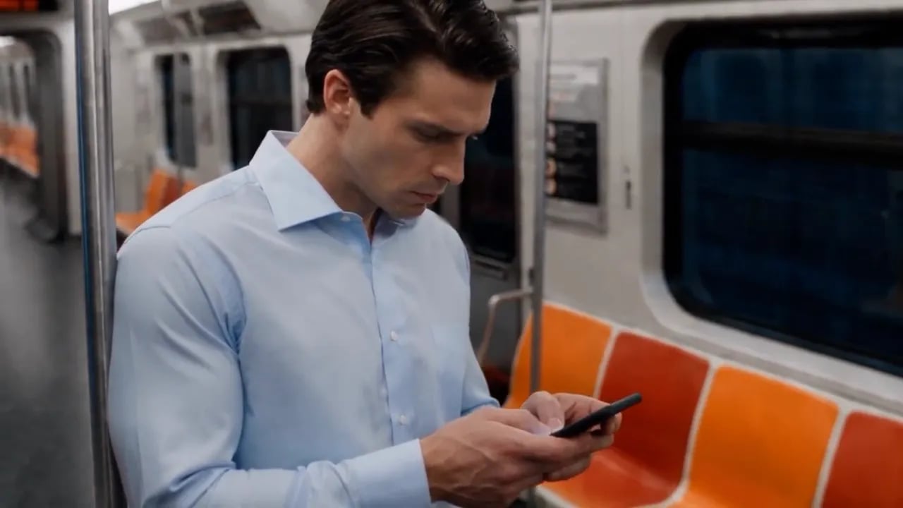 A man checks his phone on a subway car while a boy chases a soccer ball.
