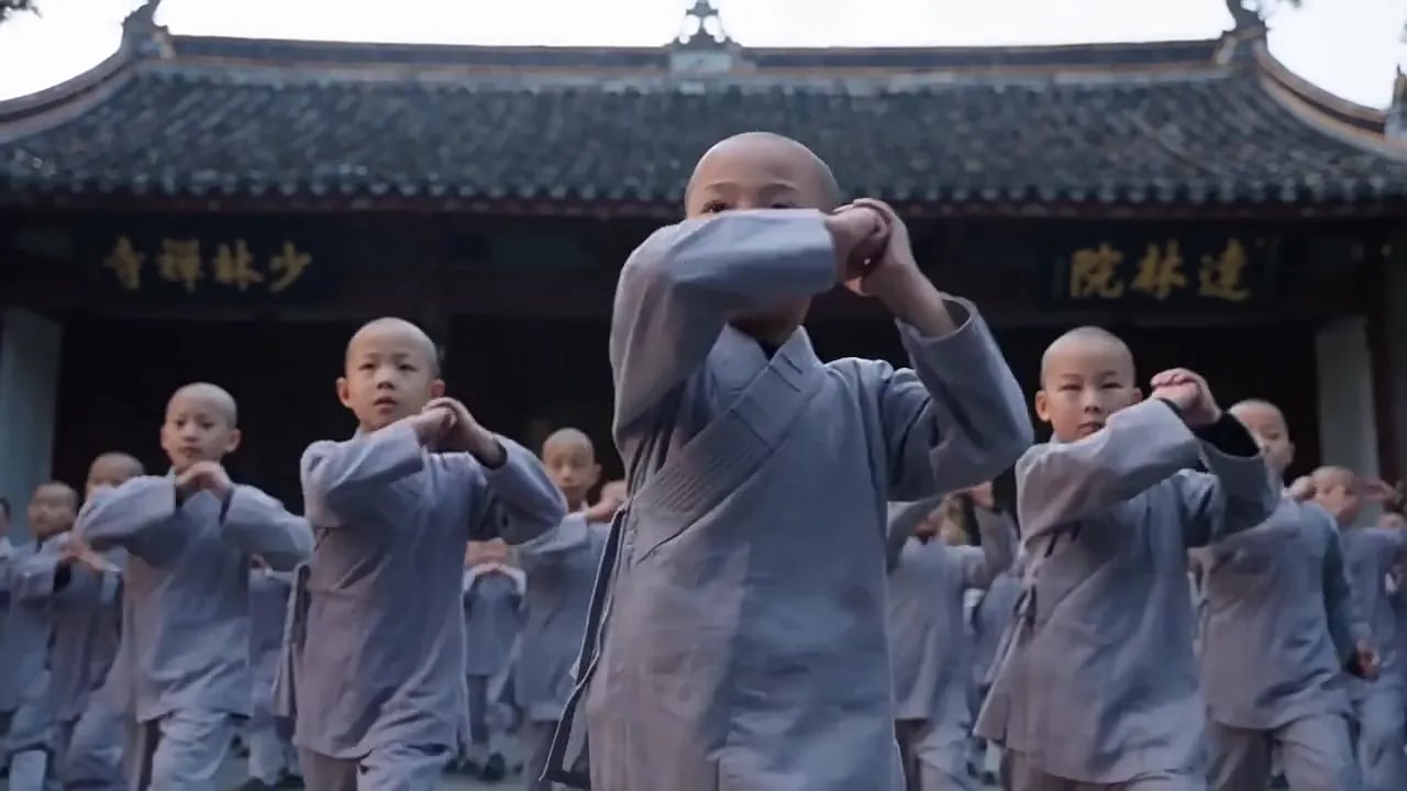 Rows of young Shaolin novice monks in grey robes train in a temple courtyard.