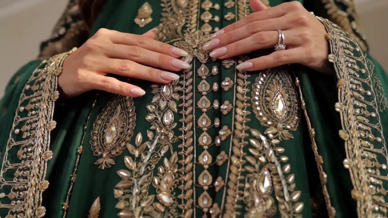 Close-up of hands resting on a green robe with gold and crystal embroidery.